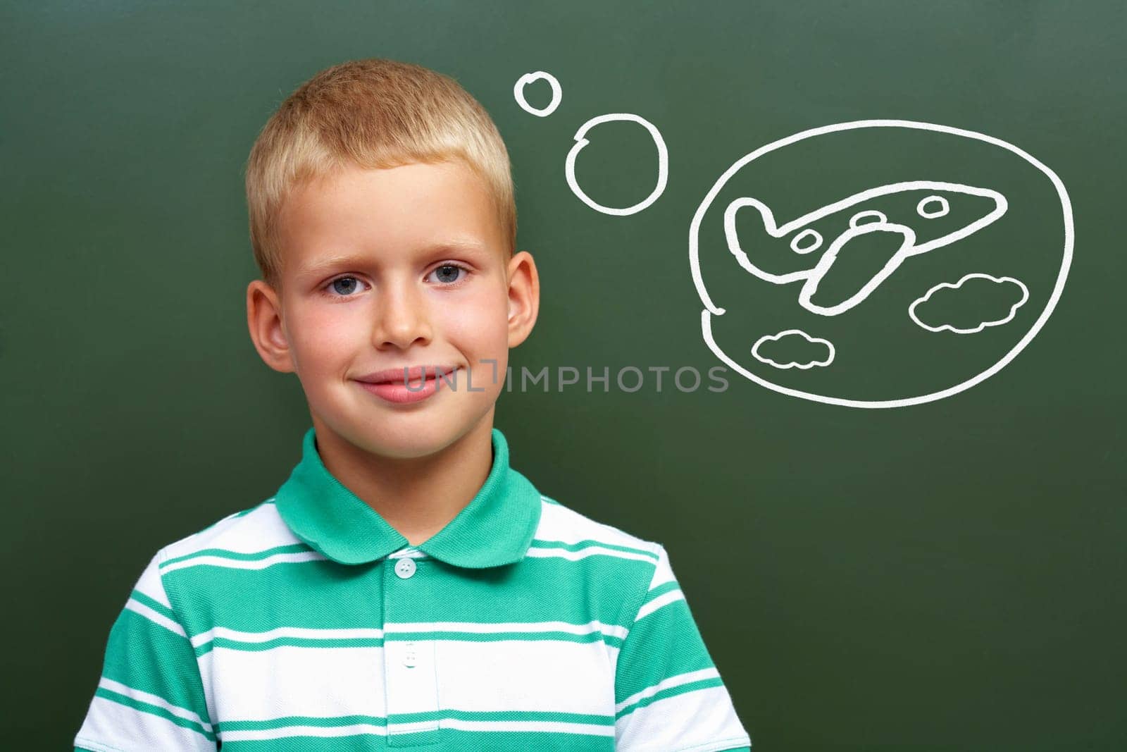 Portrait of smart lad by the blackboard thinking of airplane and looking at camera