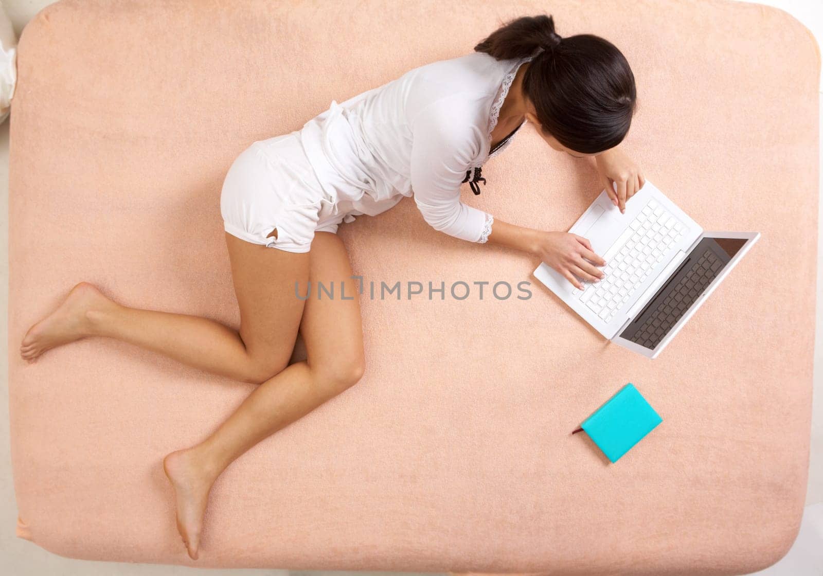 View from above of girl lying on bed and typing on laptop