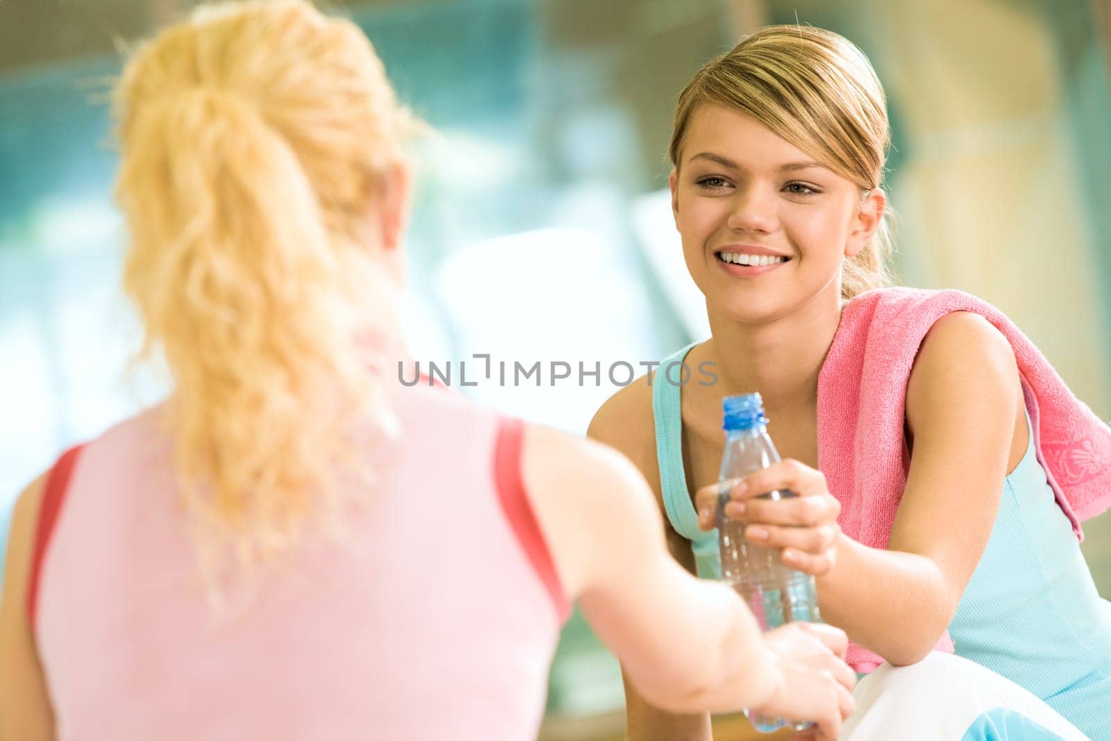 Generous girl giving bottle of water to the friend in front of her