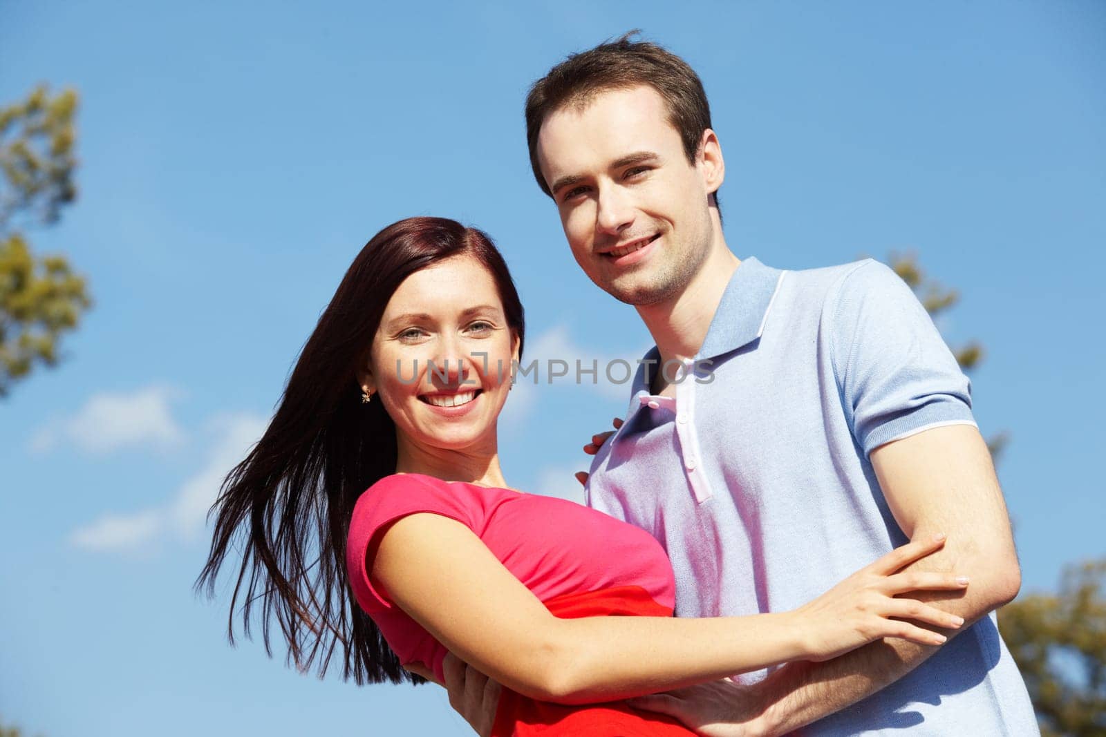 Portrait of happy couple looking at camera against blue sky