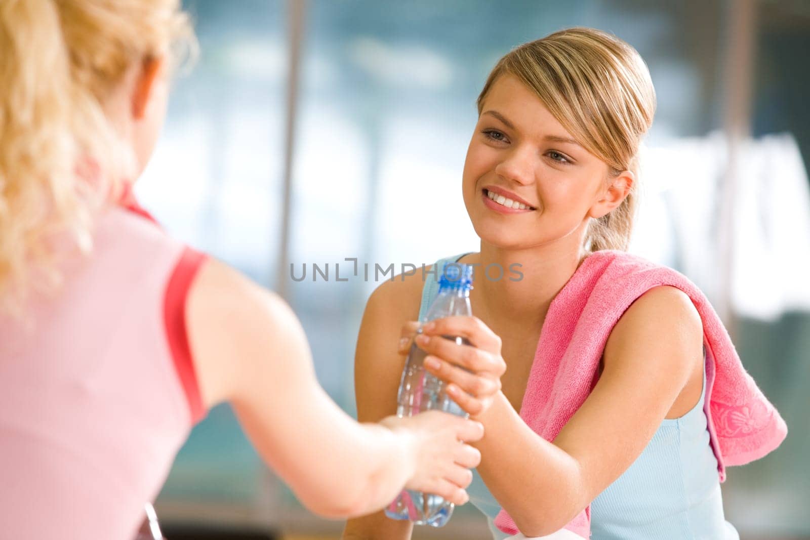 Generous girl giving bottle of water to the friend in front of her
