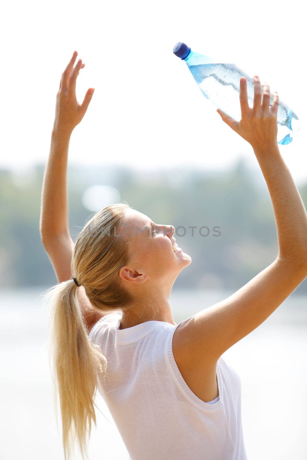 Portrait of pretty blonde with bottle of water raising arms on summer day