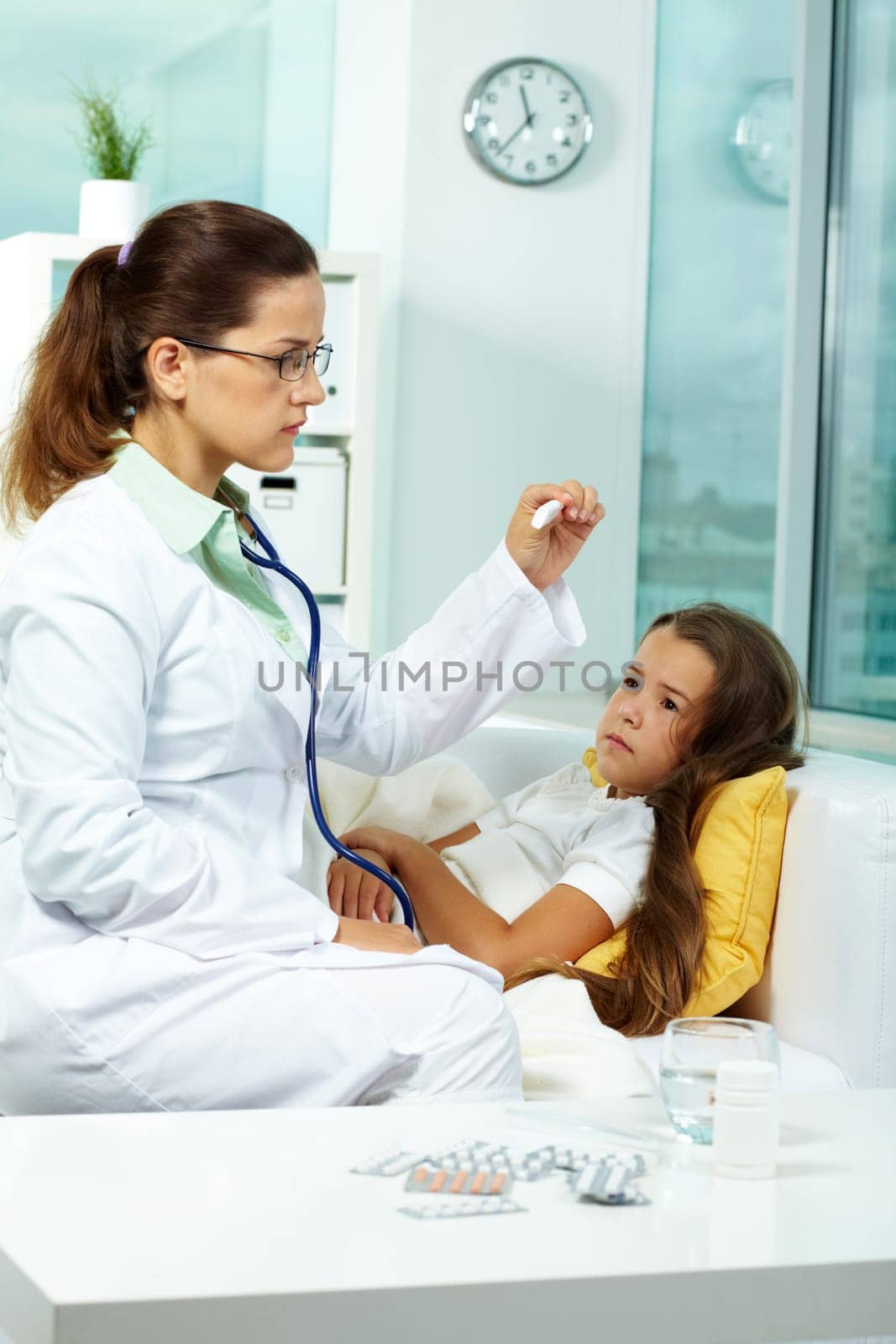 Portrait of clinician in eyeglasses looking at thermometer with sick girl lying near by