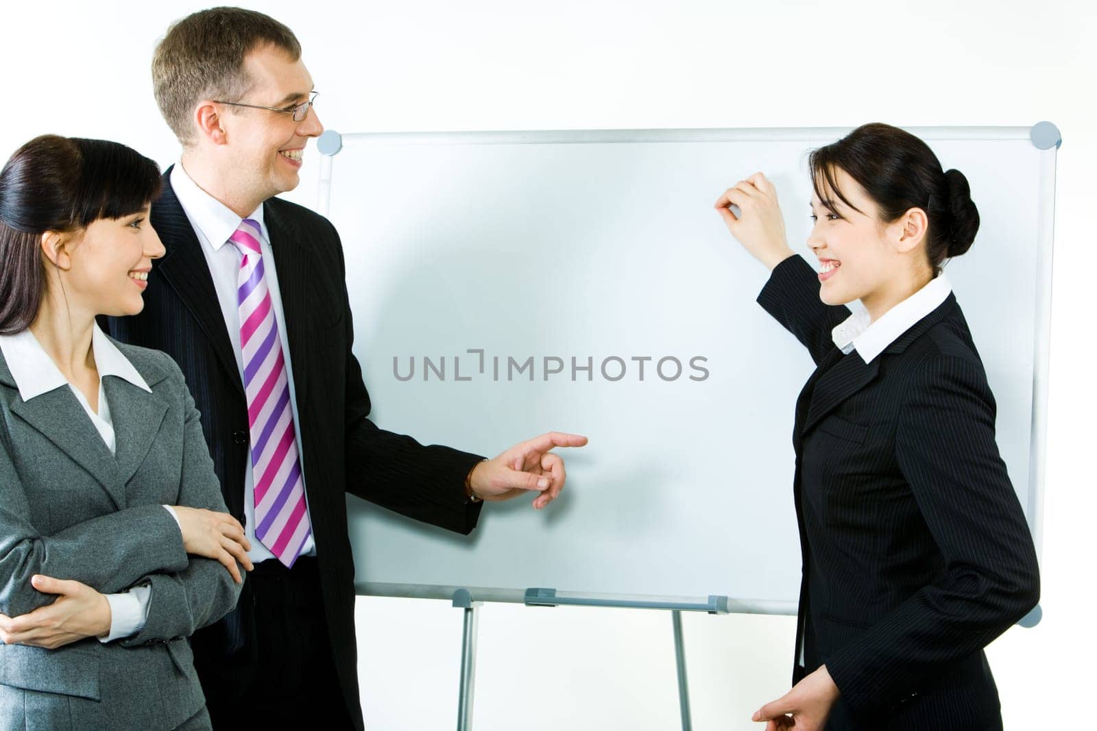 Photo of young businesswoman showing something on whiteboard with smile while her colleagues looking at it