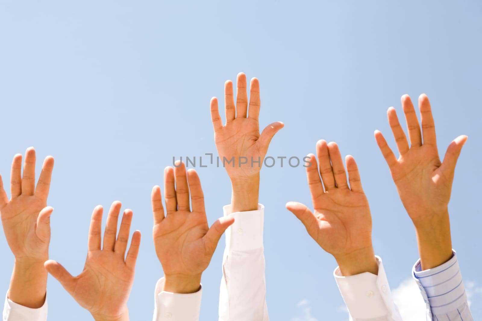 Close-up of several human hands raised against clear blue sky