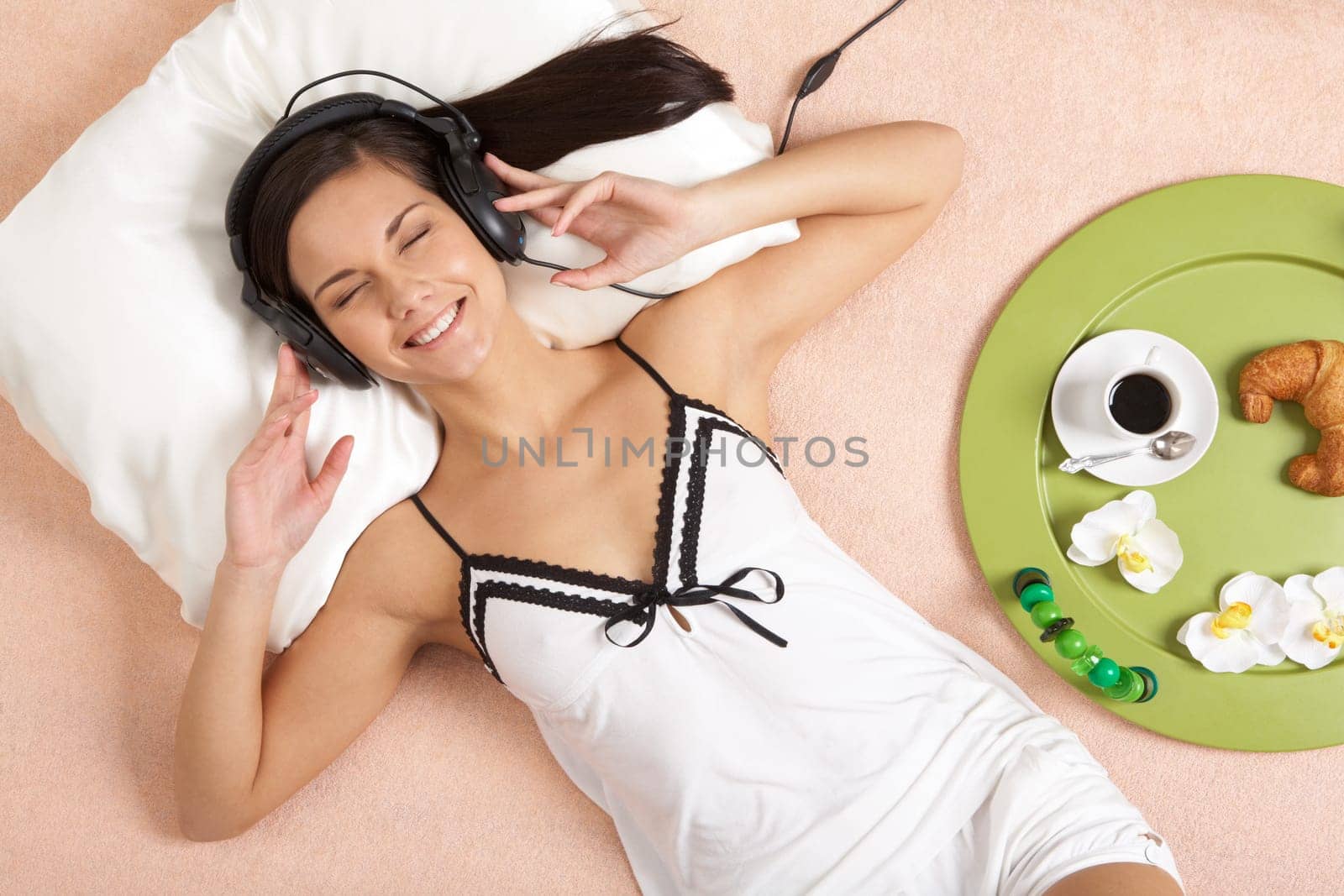 Pretty girl listening to music in headphones and smiling while lying on bed