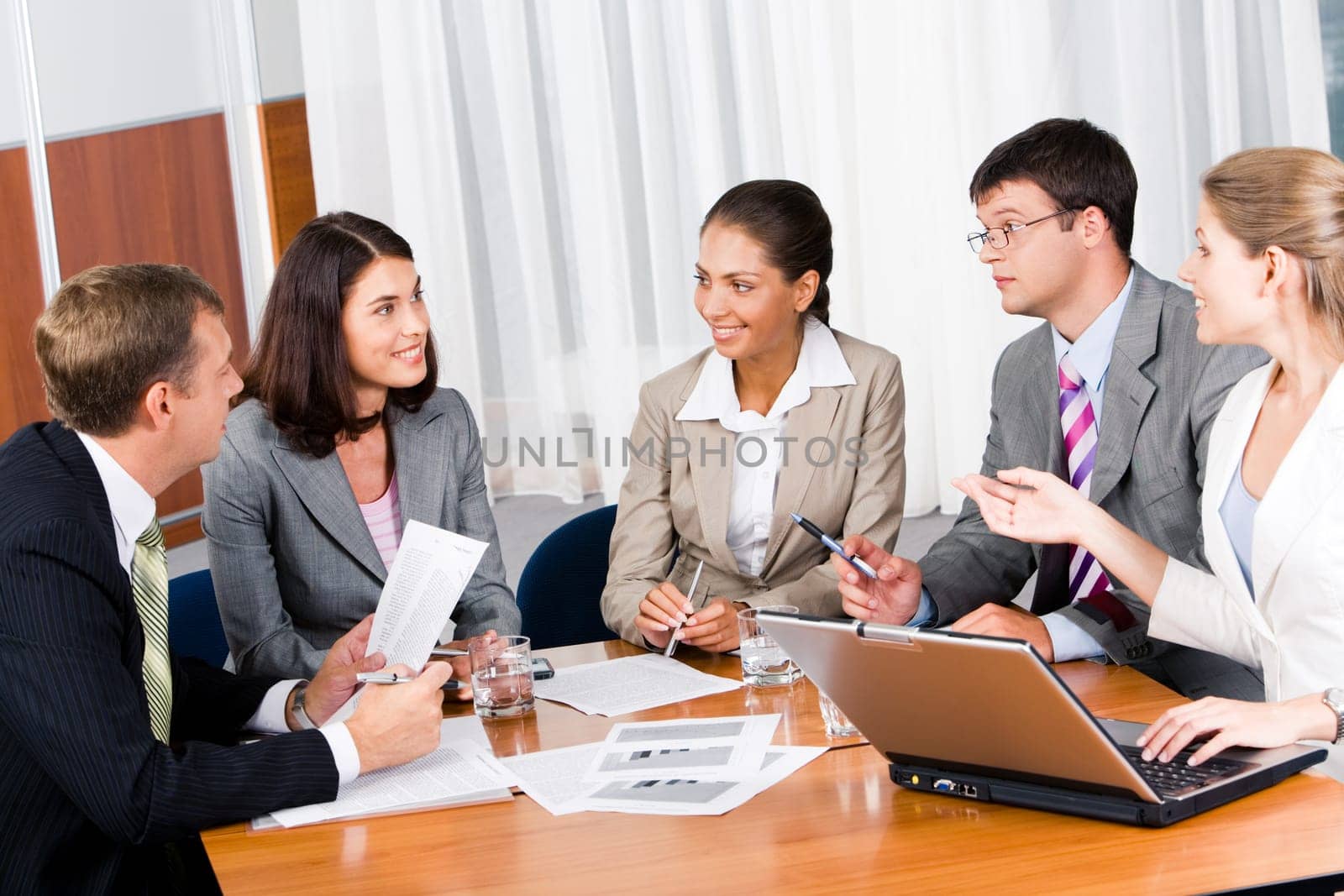 Portrait of five businesspeople sitting at the table and discussing important questions in the office