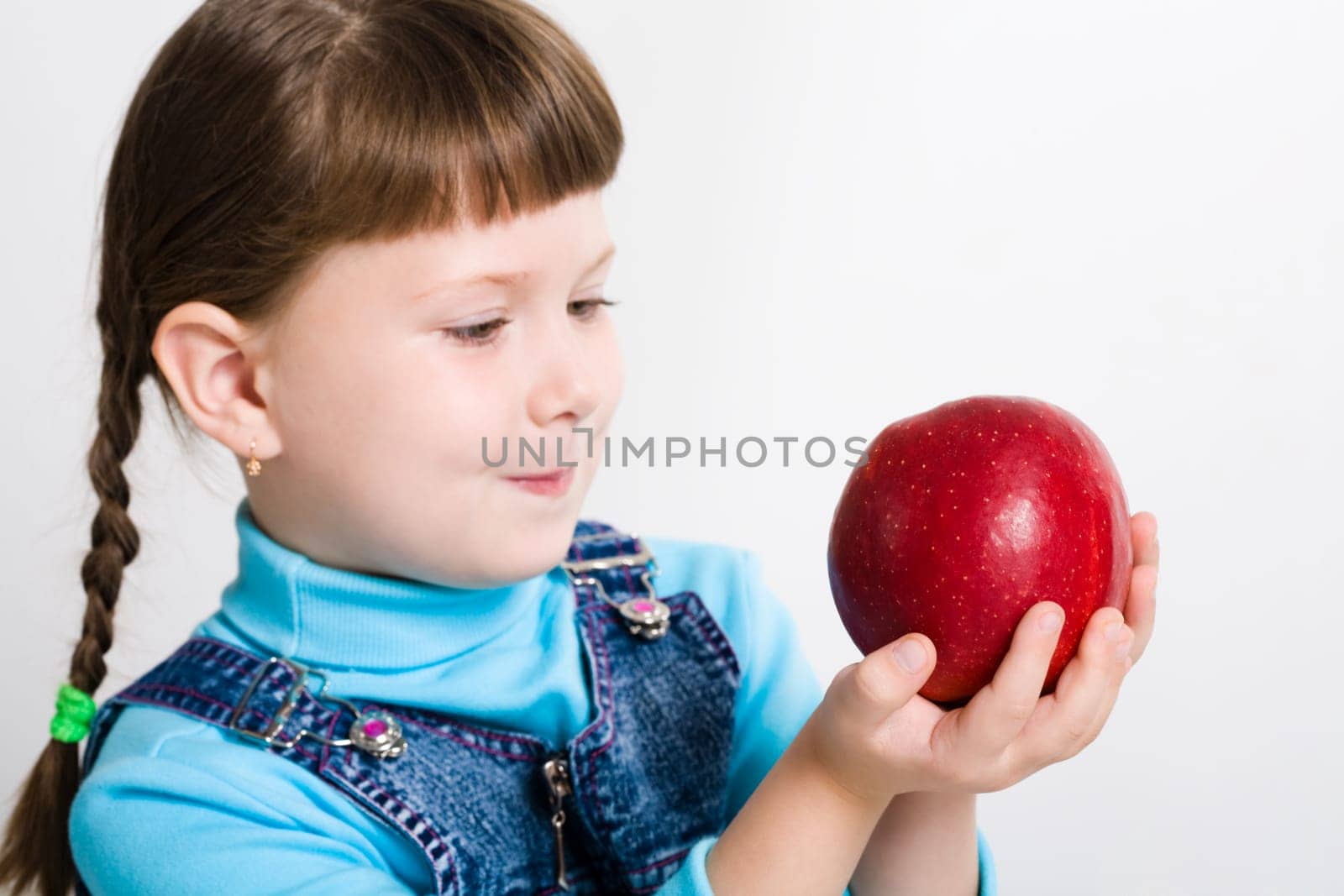Portrait of little girl holding big red apple in hands and watching at it