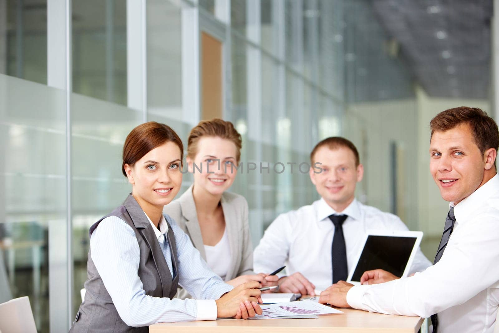 A business team of four sitting at table and looking at camera