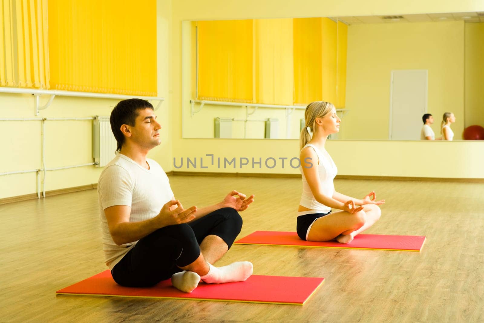 Photo of young man and woman sitting together on the floor of gym and meditating