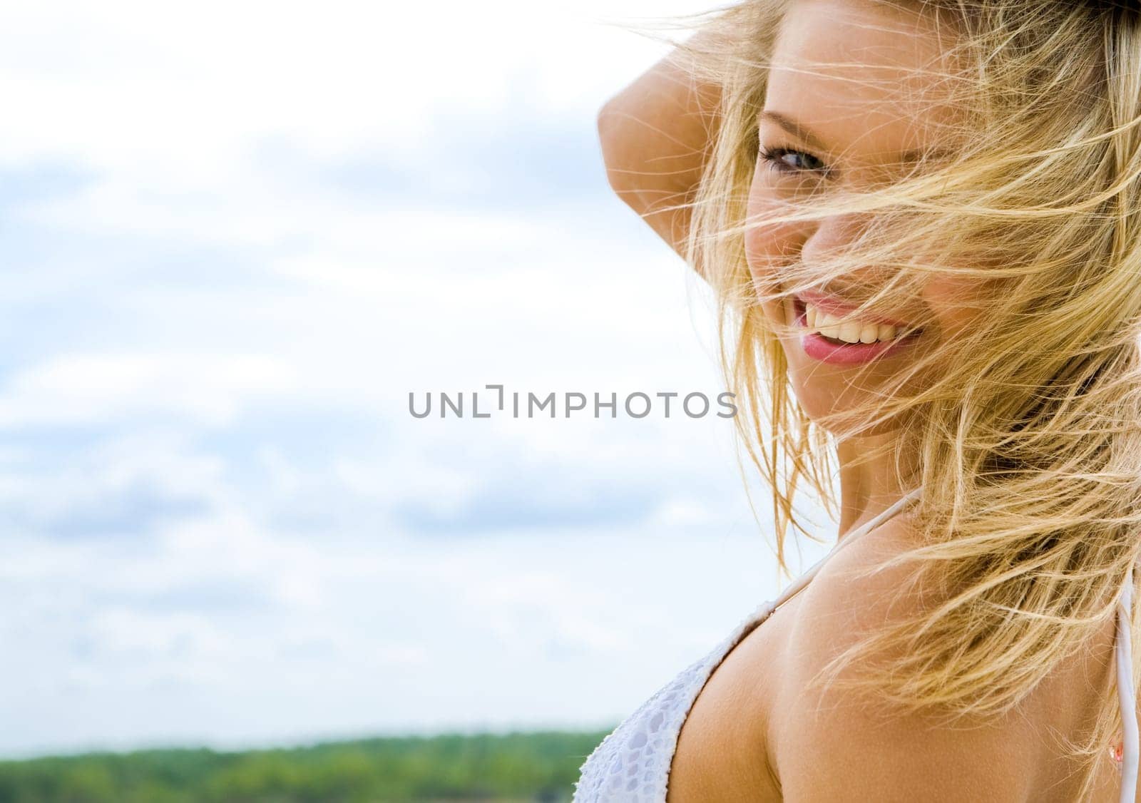 Portrait of beautiful blonde looking at camera on background of cloudy sky