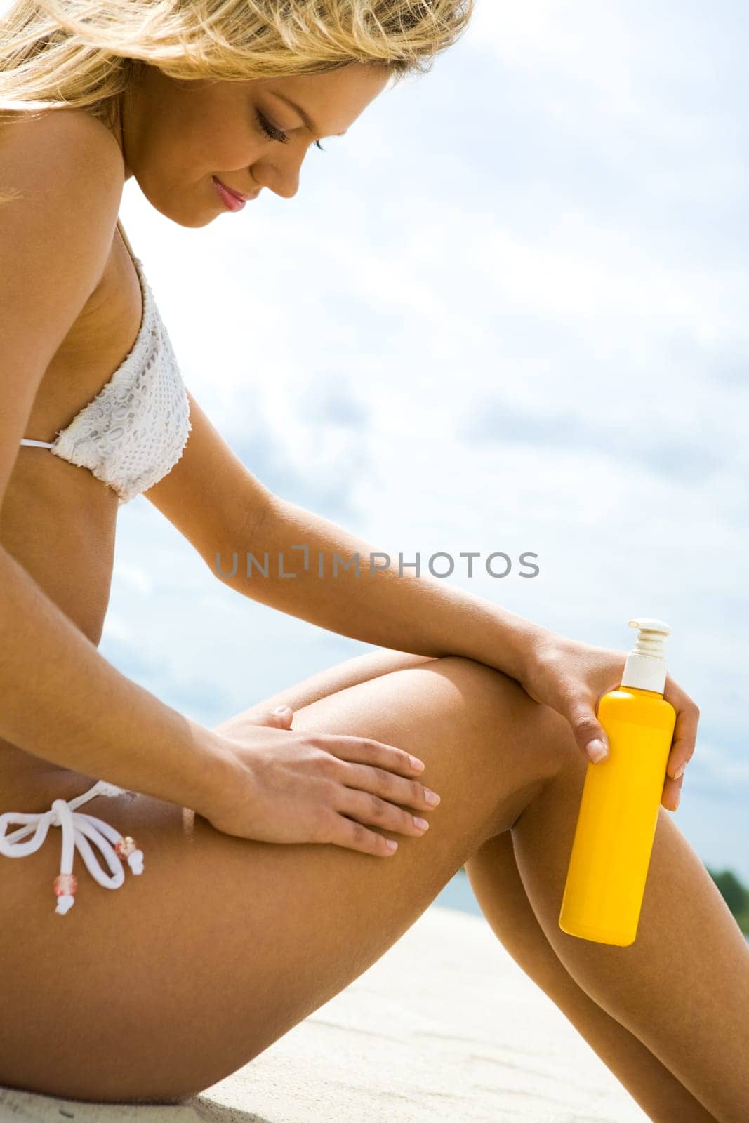 Image of female with suncare lotion sitting on sandy beach
