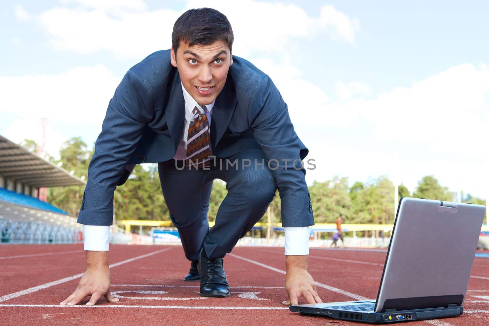 Image of businessman getting ready for race with laptop near by