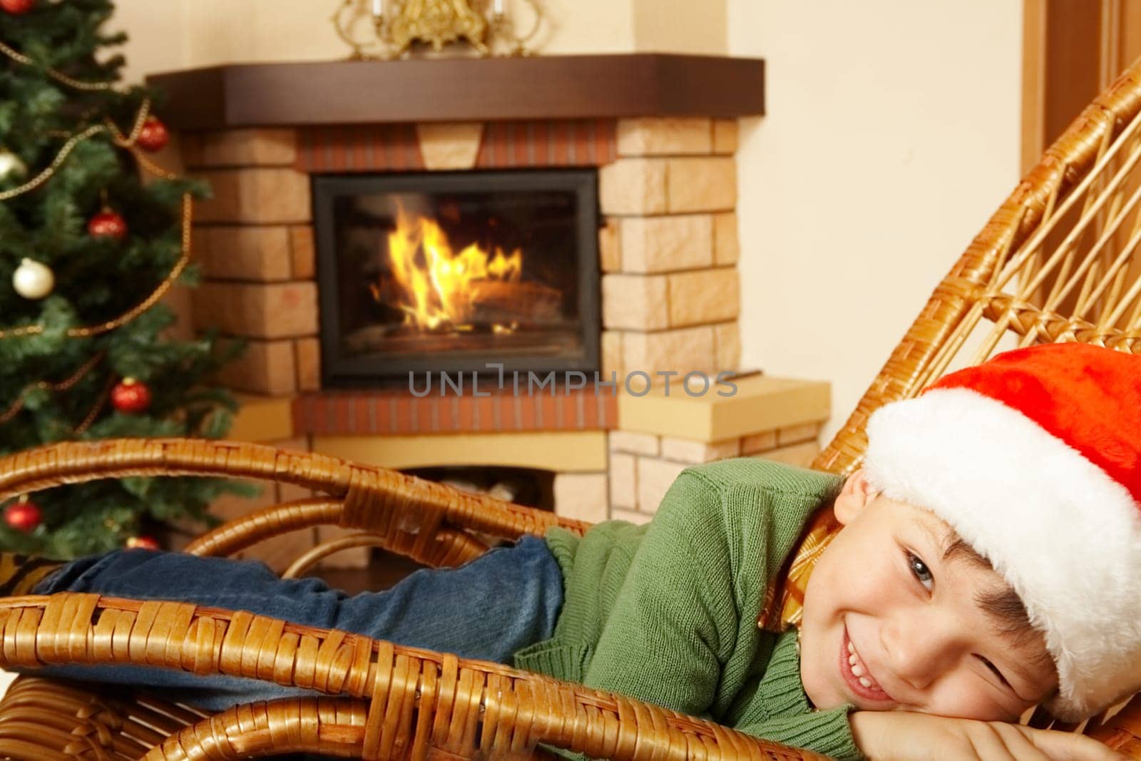 Photo of cute boy wearing santa cap pretending to sleep in rocking chair