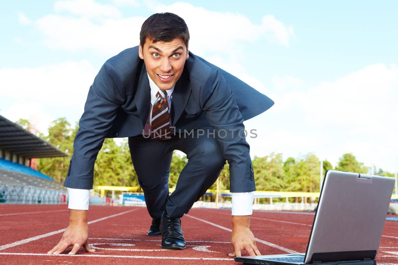 Image of businessman getting ready for race with laptop near by