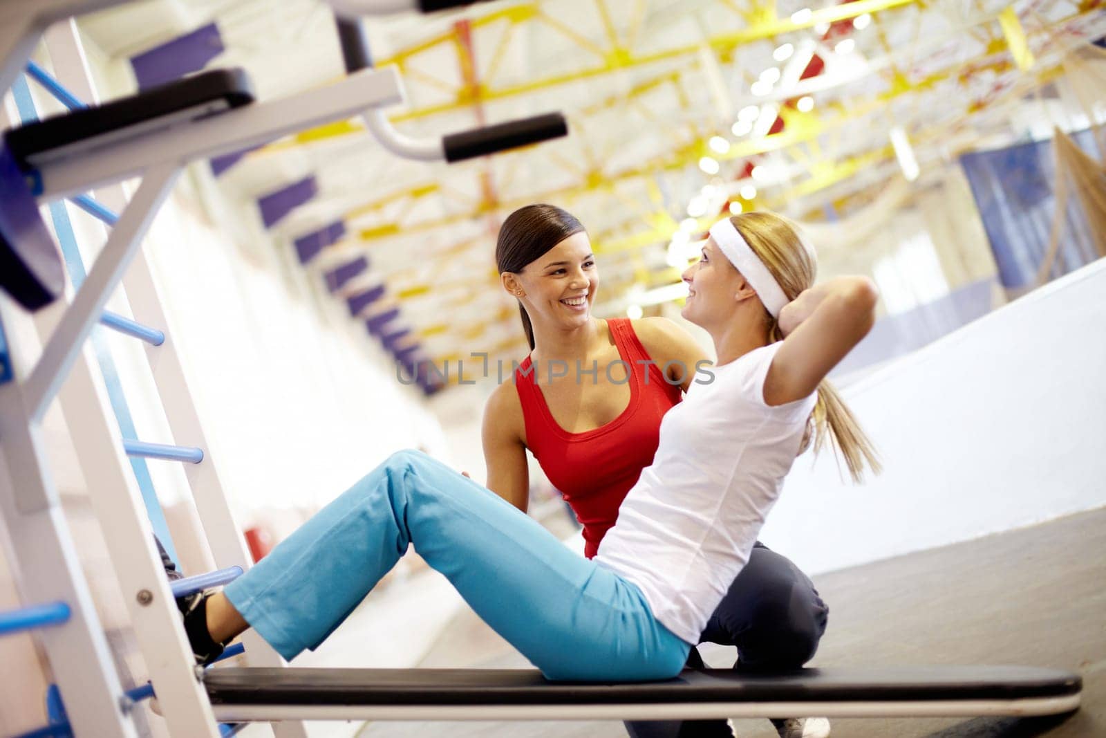 A girl pumping abdominal muscles in gym with help of her girlfriend