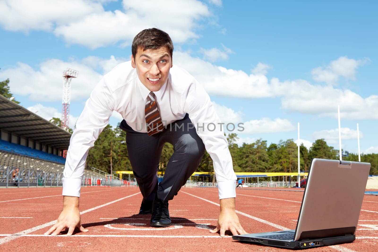 Image of handsome businessman getting ready for race at stadium