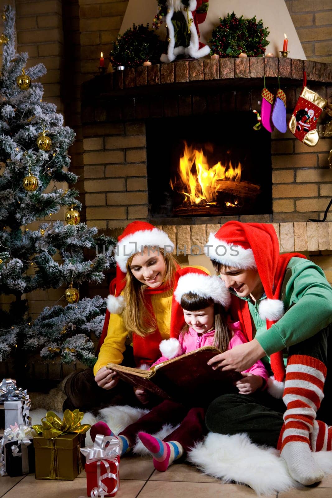 Portrait of family spending Christmas evening at reading book by fireplace