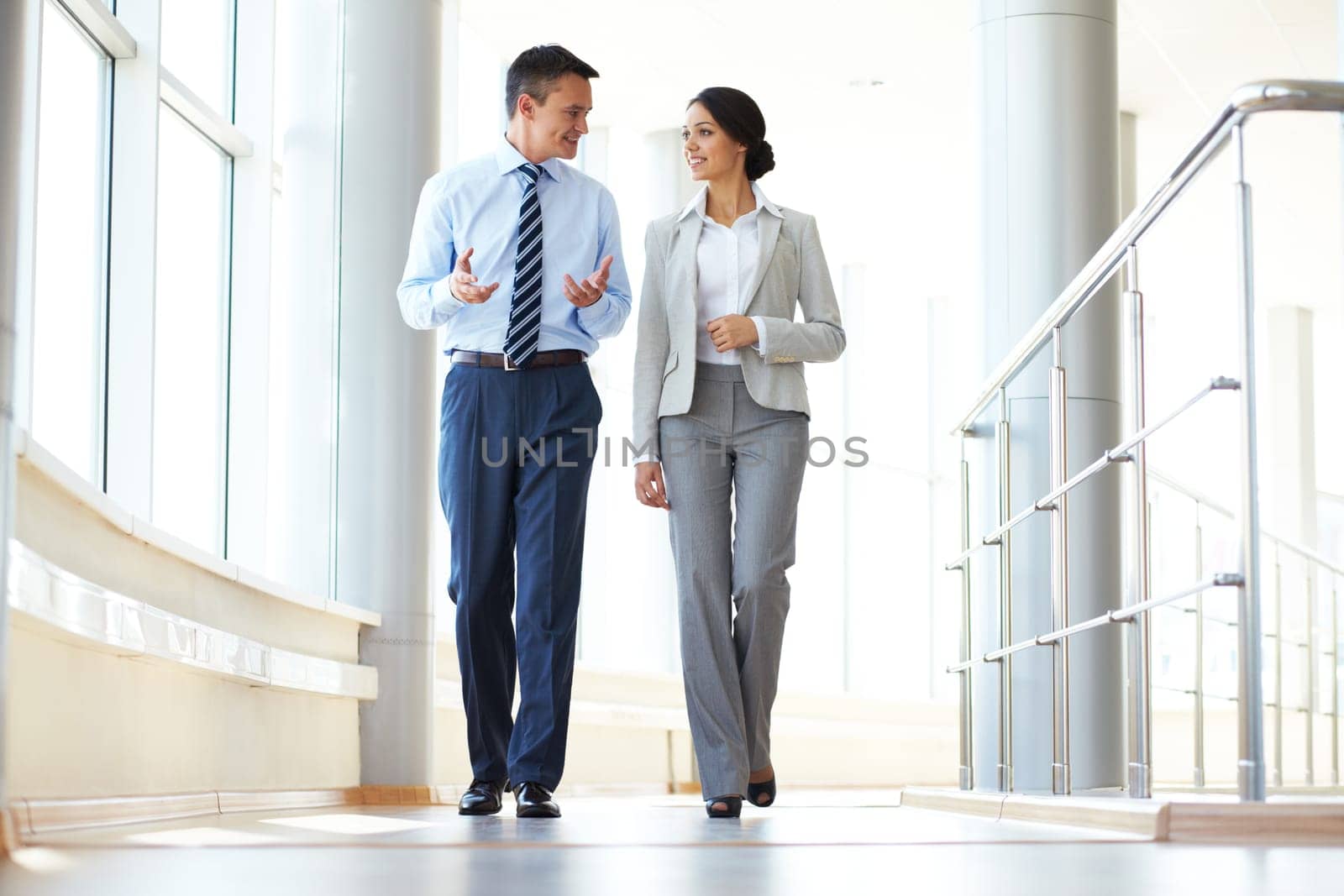 Confident business partners walking down in office building and discussing work