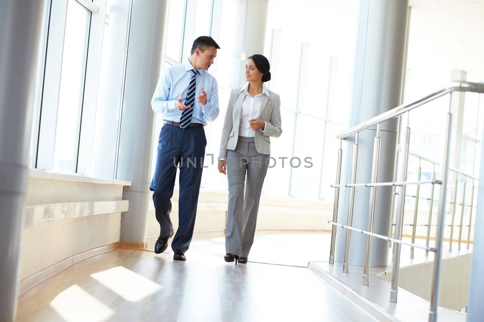 Confident business partners walking down in office building and discussing work