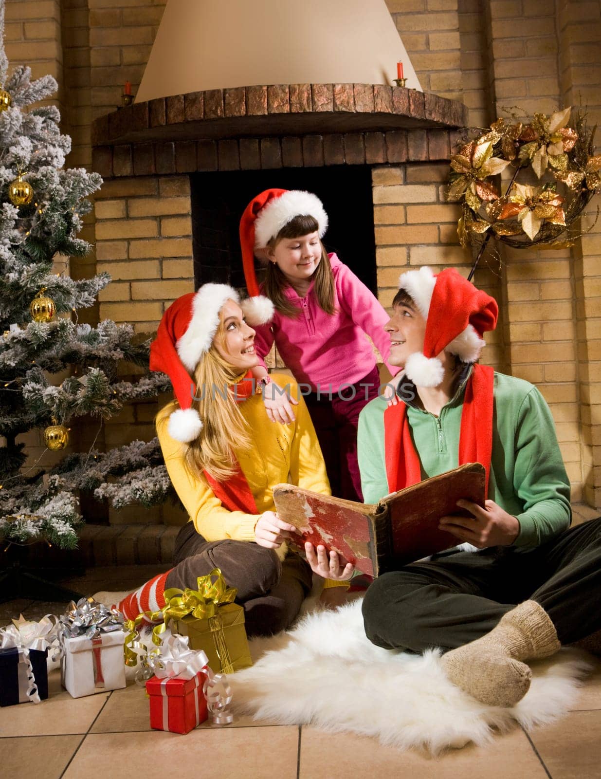 Portrait of cheerful parents sitting on white fur and looking at cute girl while reading old book