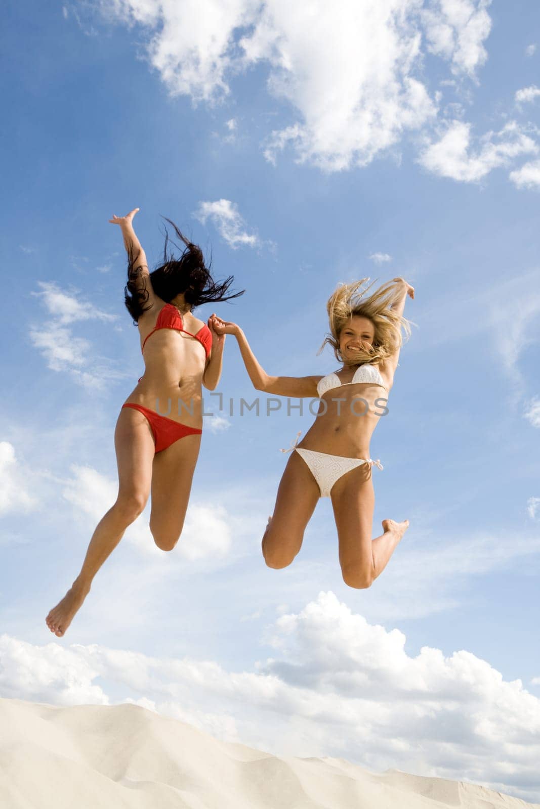 Portrait of two joyful girls leaping on sandy beach during summer vacation