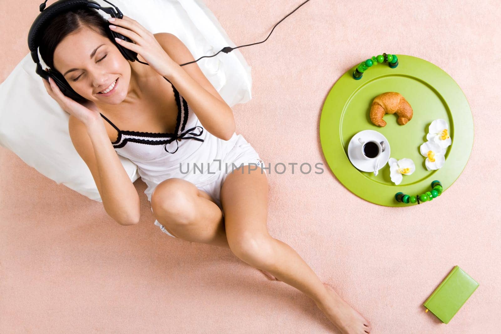 Above view of happy girl sitting on bed and listening to music in headphones