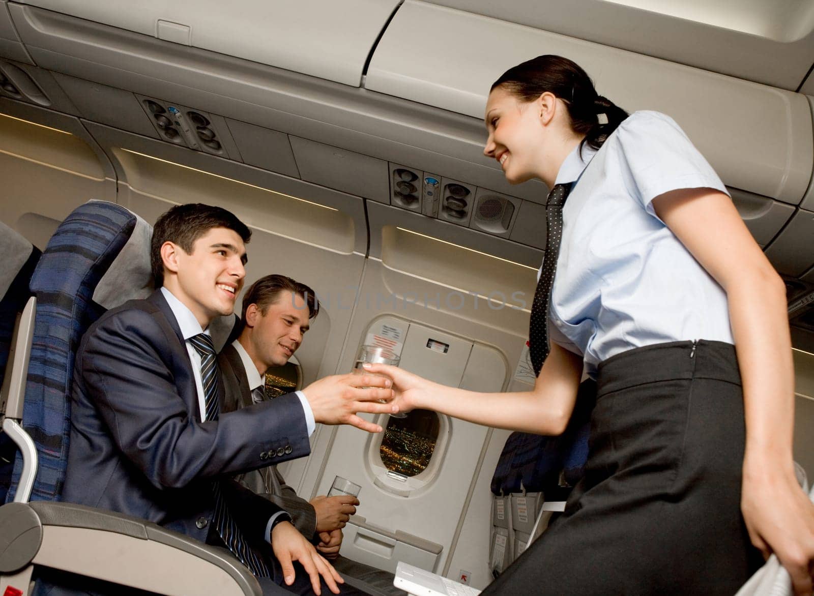 Kind stewardess giving glass of water to young businessman in airplane
