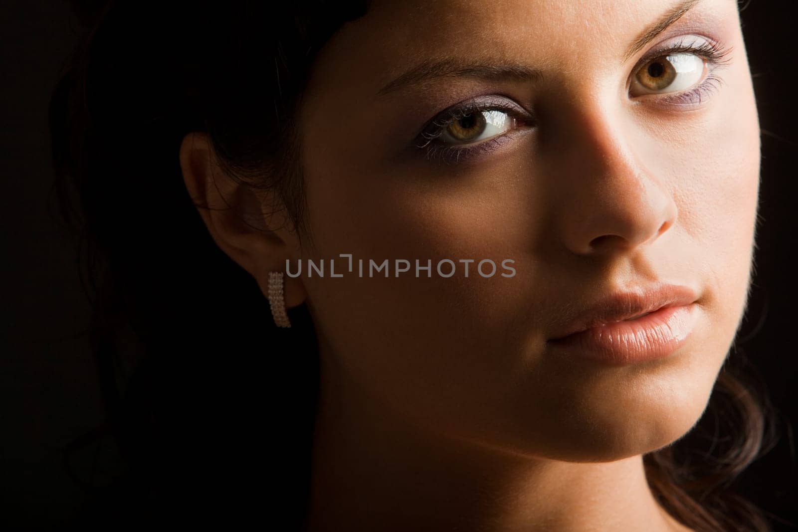Face of luxurious woman with brown eyes looking at camera over black background