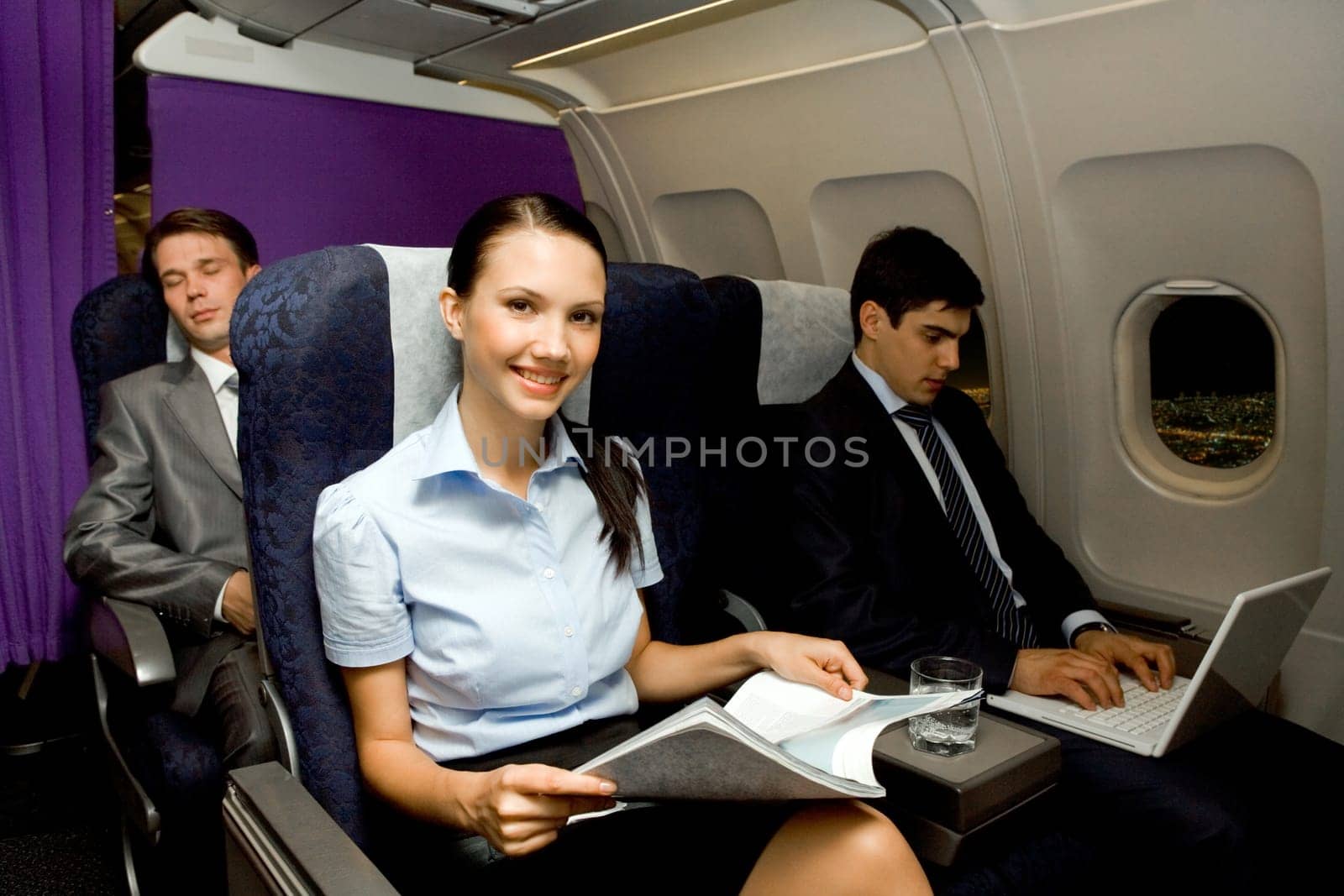 Image of pretty girl with magazine looking at camera while handsome man typing next to her