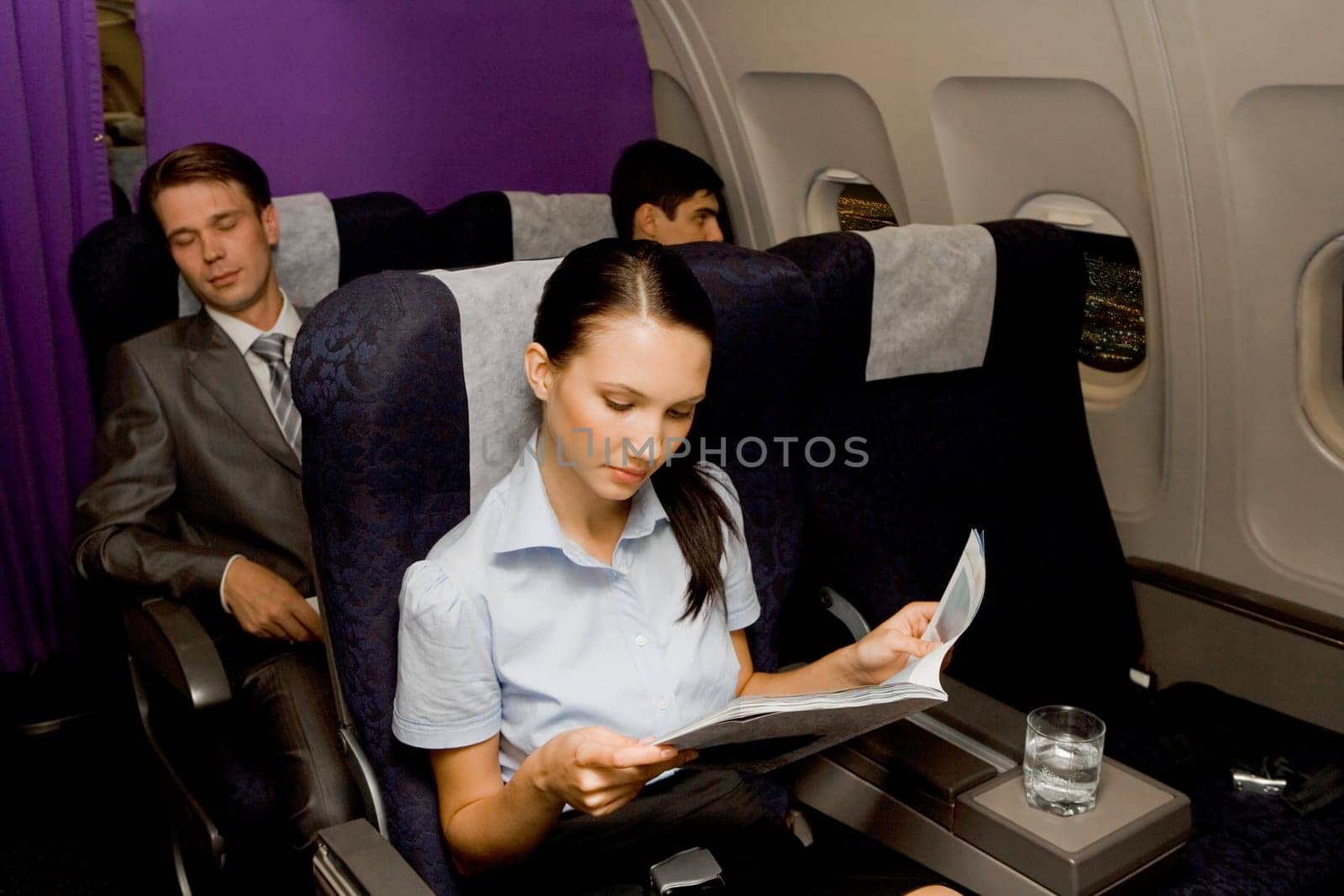 Image of pretty girl reading magazine in airplane with sleeping men behind