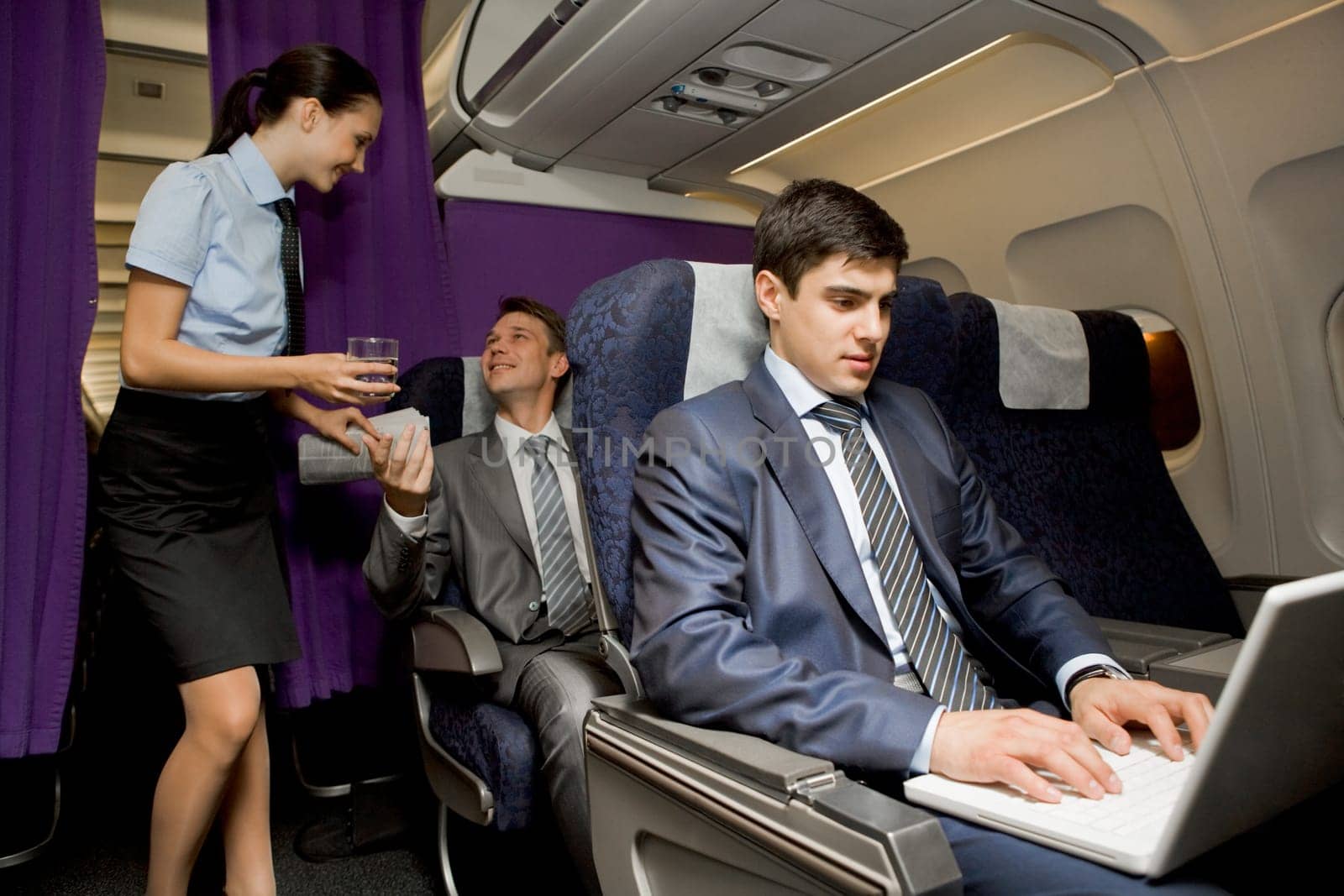 Image of busy male typing on laptop with pretty stewardess giving glass of water to successful businessman on background