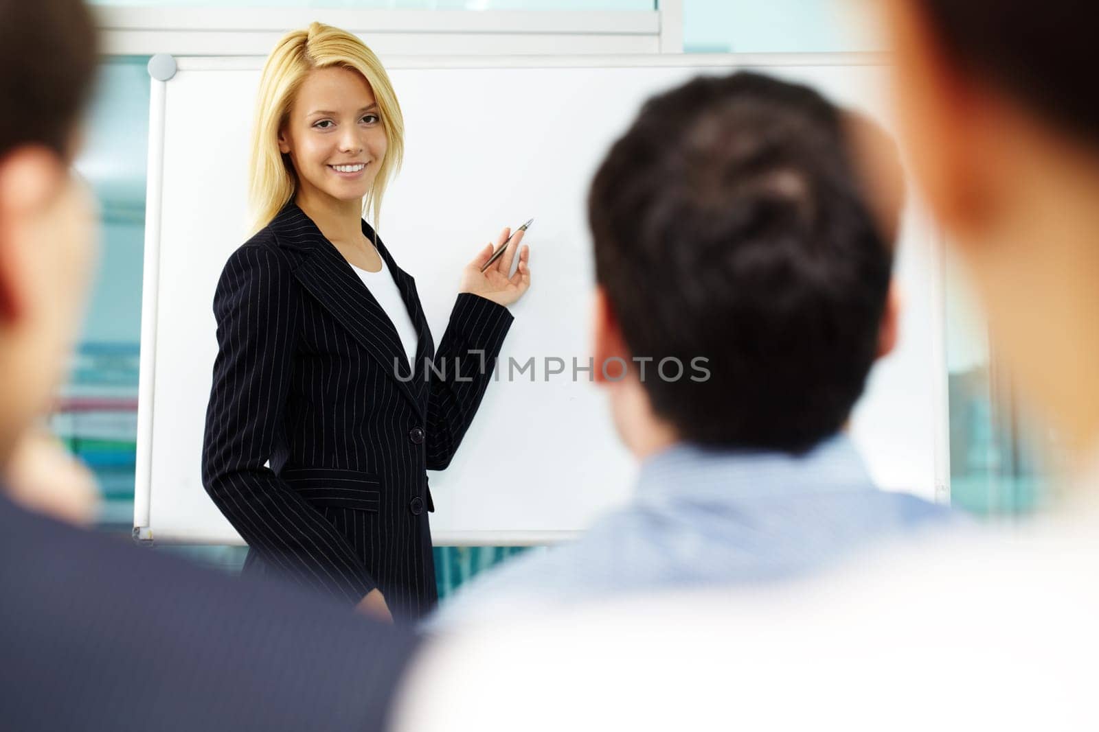 Pretty manager pointing at whiteboard while colleagues listening to her