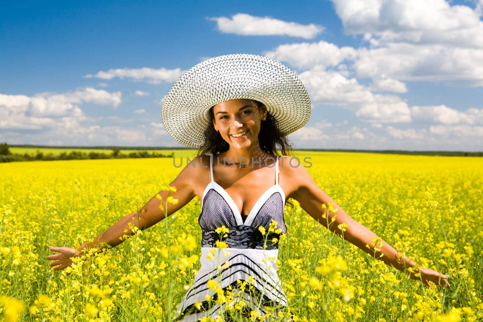 Portrait of pretty woman standing in the middle of yellow meadow and looking at camera with smile