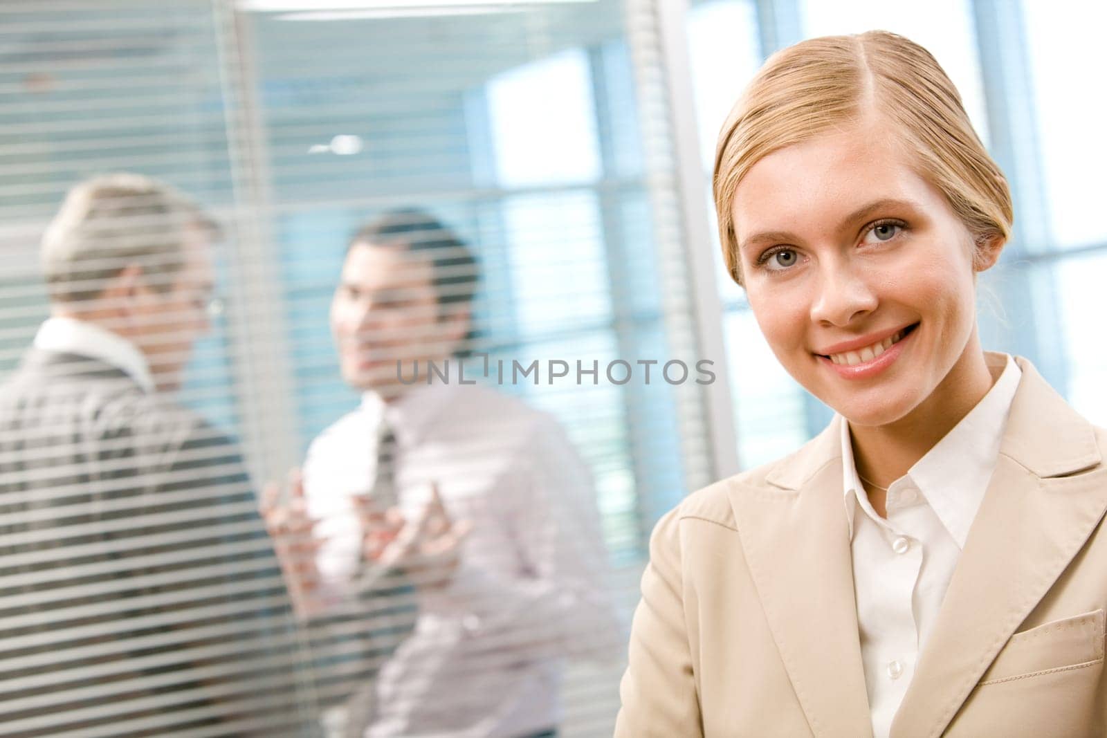 Portrait of happy businesswoman smiling at camera on background of interacting men