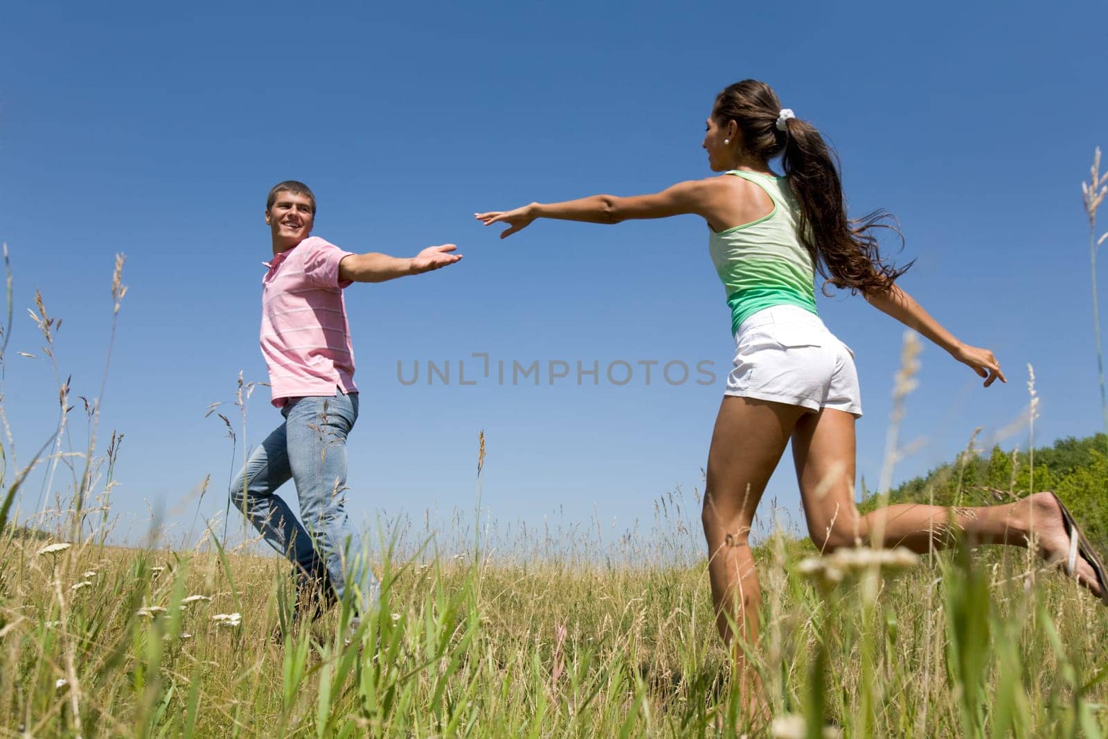 Photo of young couple running down green grass in the countryside