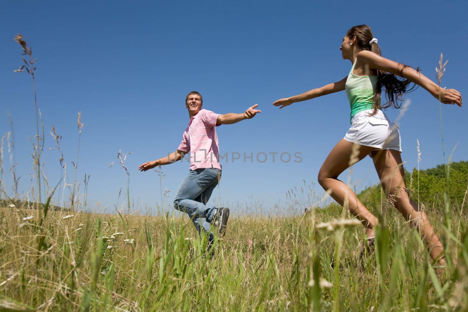 Attractive dates having fun while running down green field during weekend