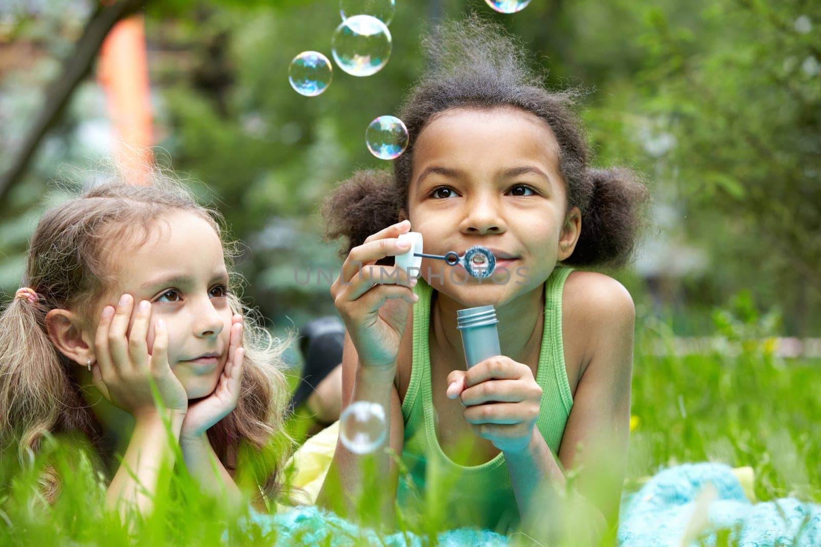 Portrait of cute girl blowing soap bubbles with her friend near by