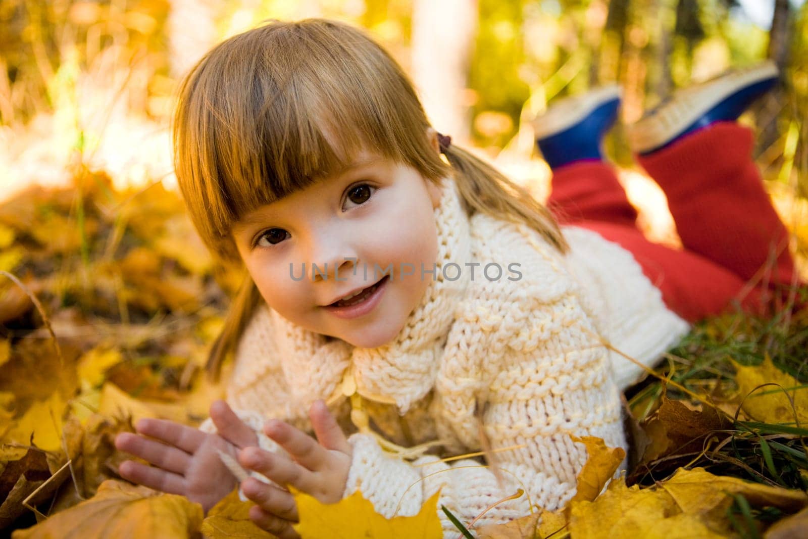 Small adorable girl lying on golden leaved ground in autumn and enjoying herself