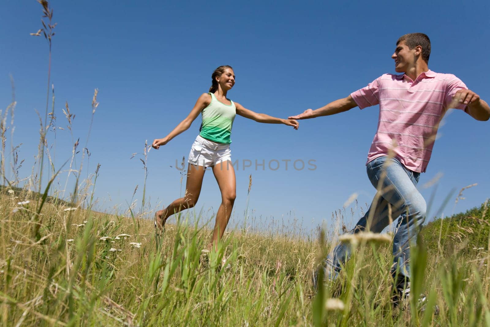 Photo of young couple running down green grass in the countryside