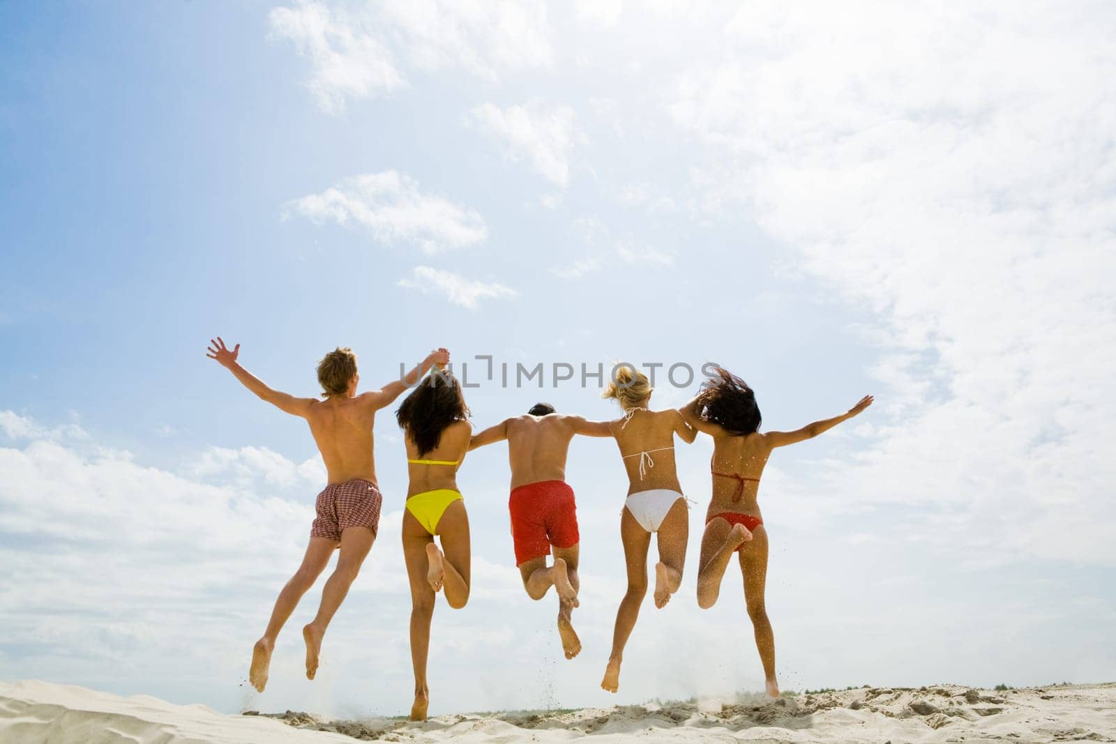 Rear view of friends holding by hands and jumping on sand