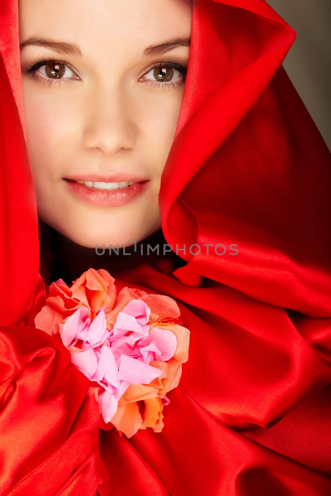 Gorgeous woman in red satin holds flower looking at camera