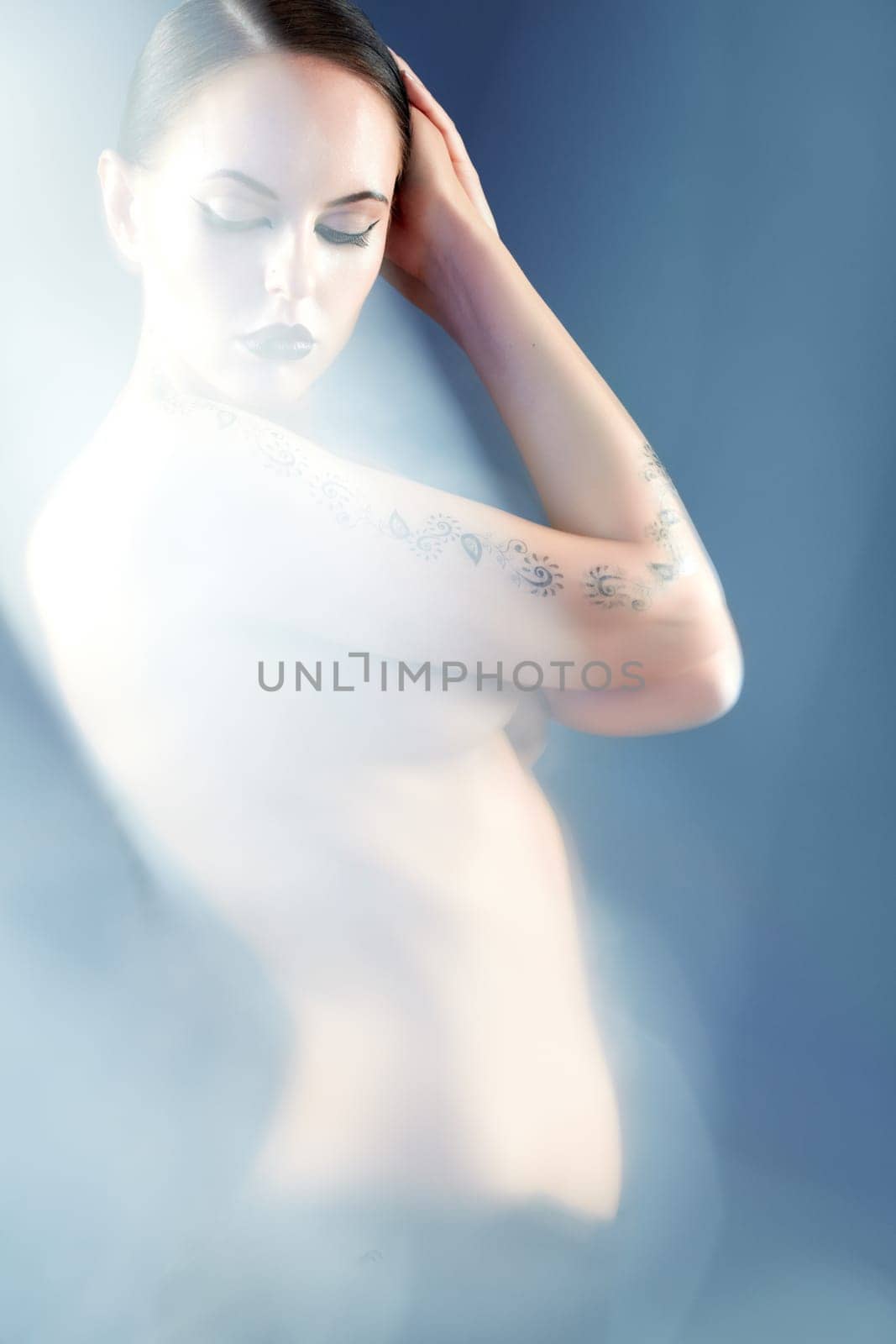 Portrait of naked woman with tattoo surrounded by mist