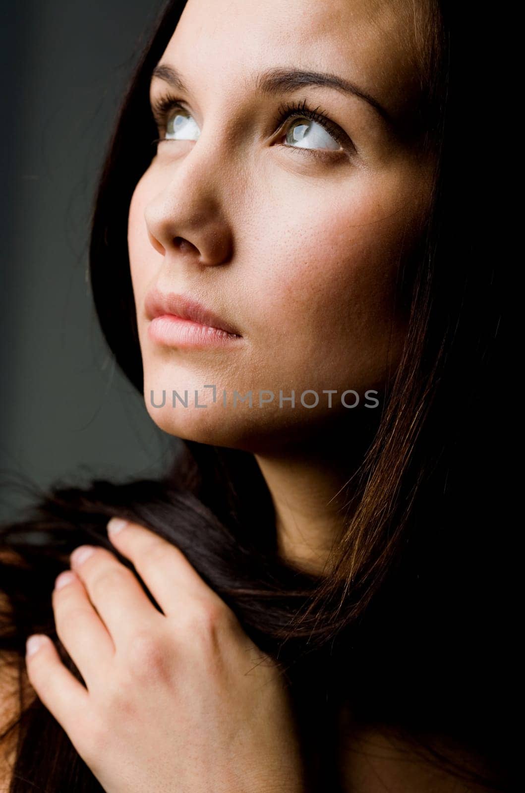 Image of young female with dark hair touching it by hand and looking upwards