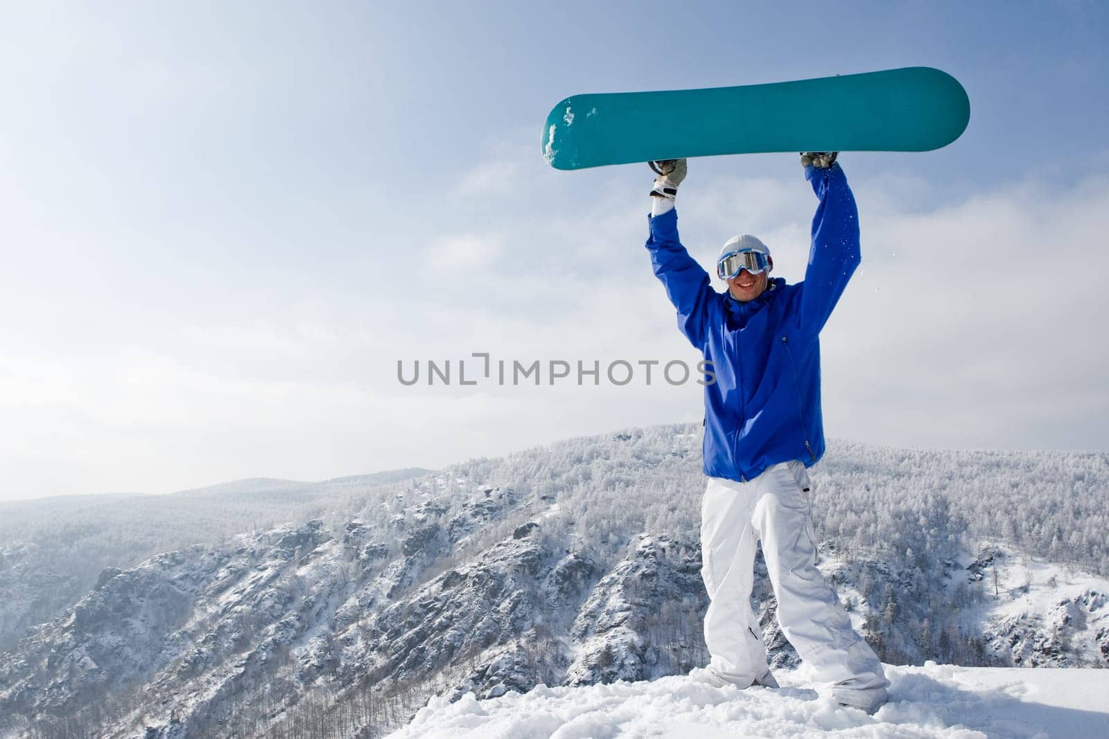 Portrait of joyful sportsman with snowboard standing on top of mount