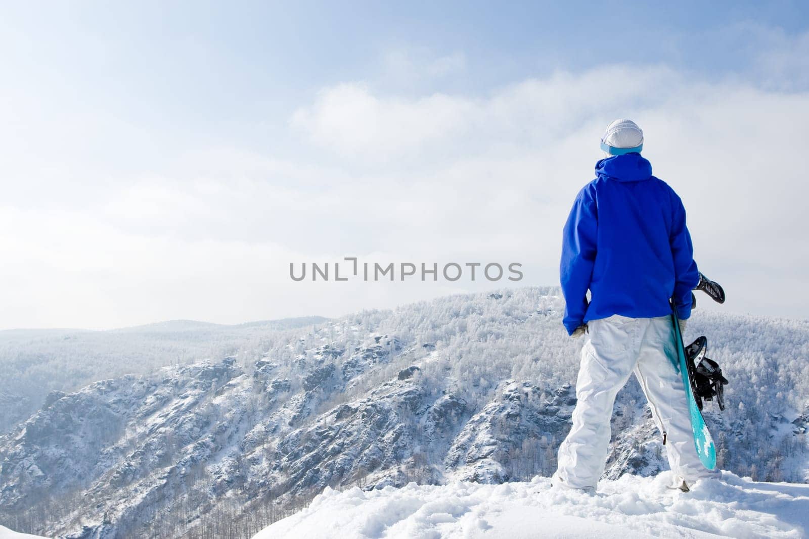 Rear view of sportsman with snowboard standing on top of mount