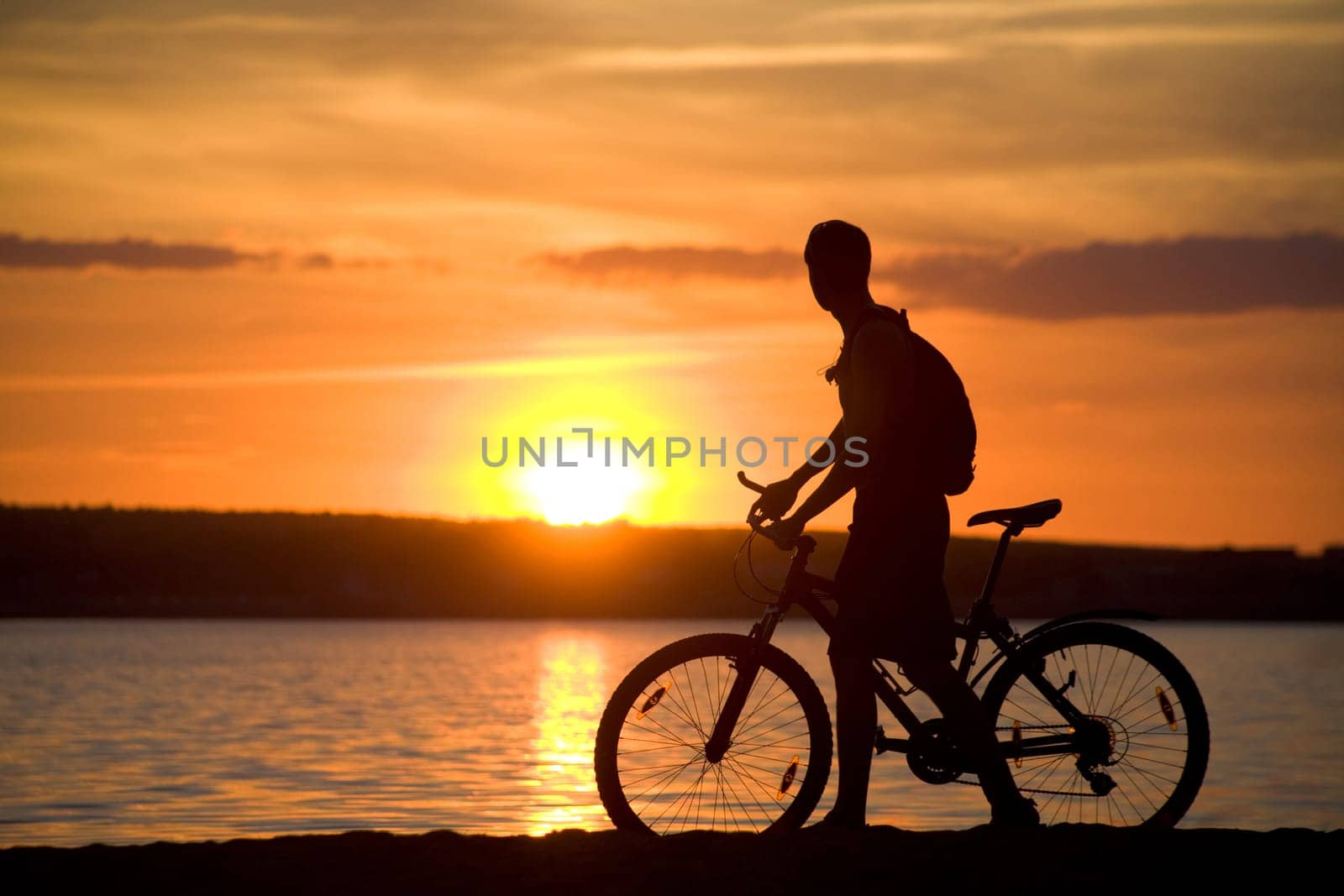 Silhouette of man riding bicycle with beautiful lake near by at sunset