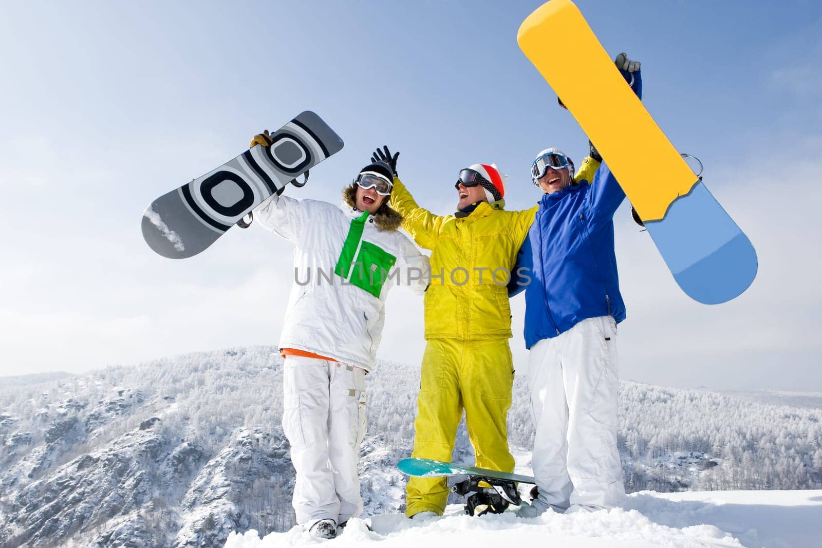 Portrait of three successful snowboarders raising their arms on mountain top