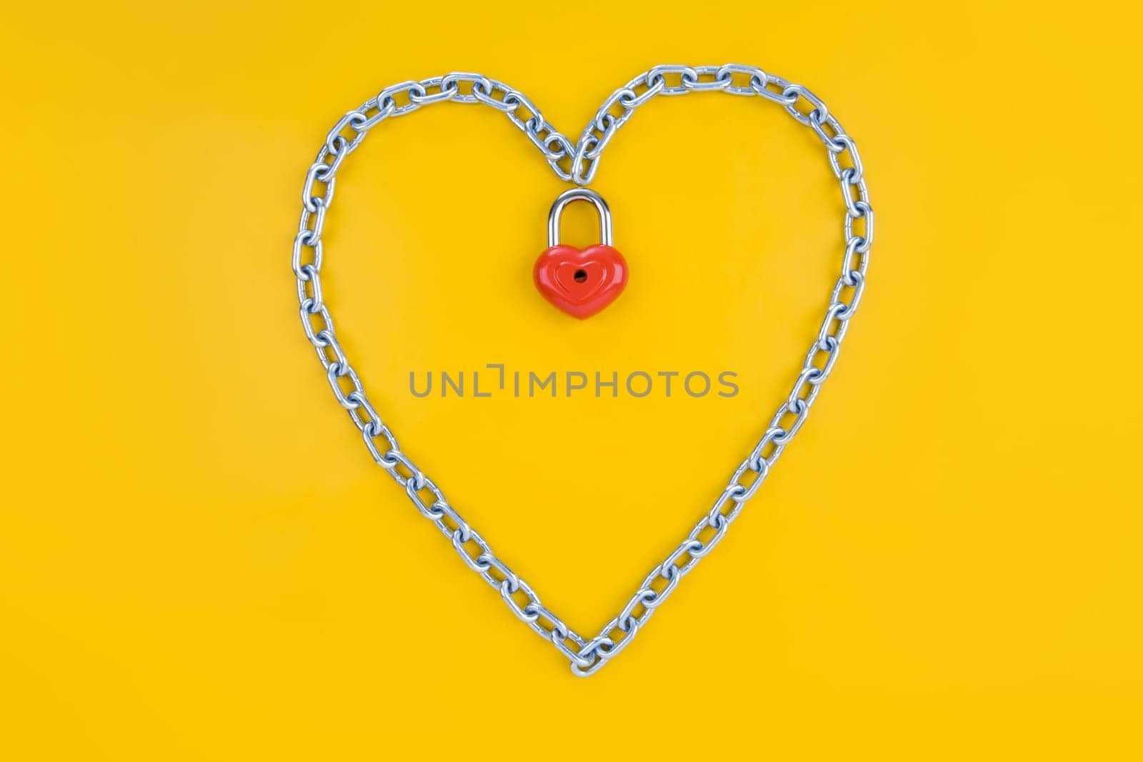 Image of metallic heart made of chain with lock on a yellow background