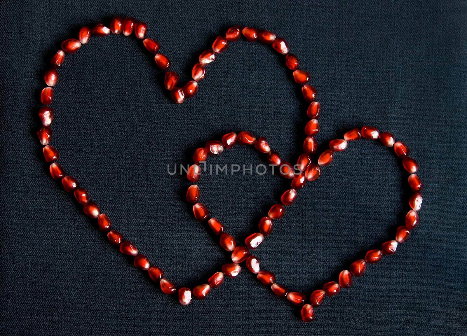 Image of two hearts made up of pomegranate grains over dark fabric